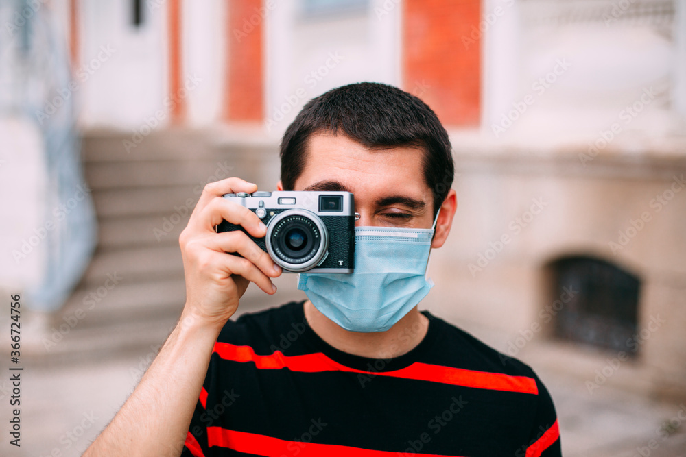Man with mask taking photos with reflex camera in summer on the street