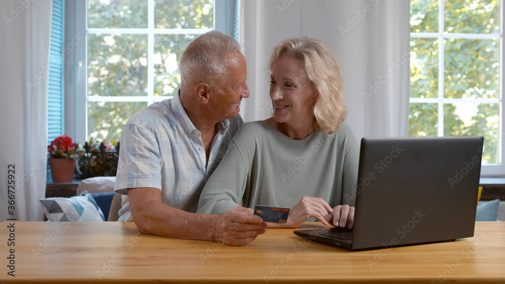 smiling mature couple using credit card and laptop shopping online smiling mature couple using credit card and laptop shopping online