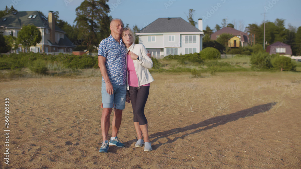 Senior couple embracing on beach near country house enjoying vacation