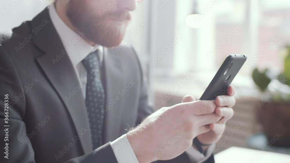 Close up arc shot of young bearded businessman in formalwear typing on smartphone during workday in the office Close up arc shot of young bearded businessman in formalwear typing on smartphone during workday in the office