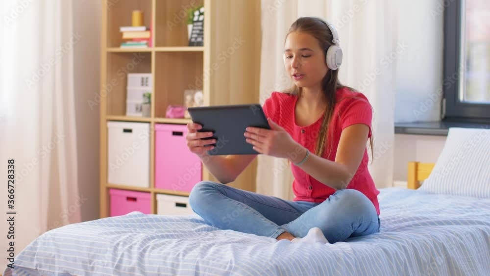 children, technology and communication concept - smiling teenage girl in headphones having video call on tablet computer sitting on bed at home children, technology and communication concept - smiling teenage girl in headphones having video call on tablet computer sitting on bed at home