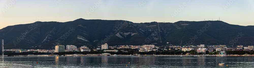 Ultra-wide panorama and evening view of the resort city of Gelendzhik, many buildings at the foot of majestic mountains, a beautiful summer landscape and the beauty of nature.