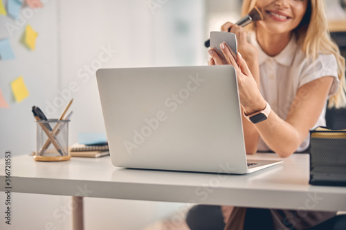 Smiling young woman doing makeup at work