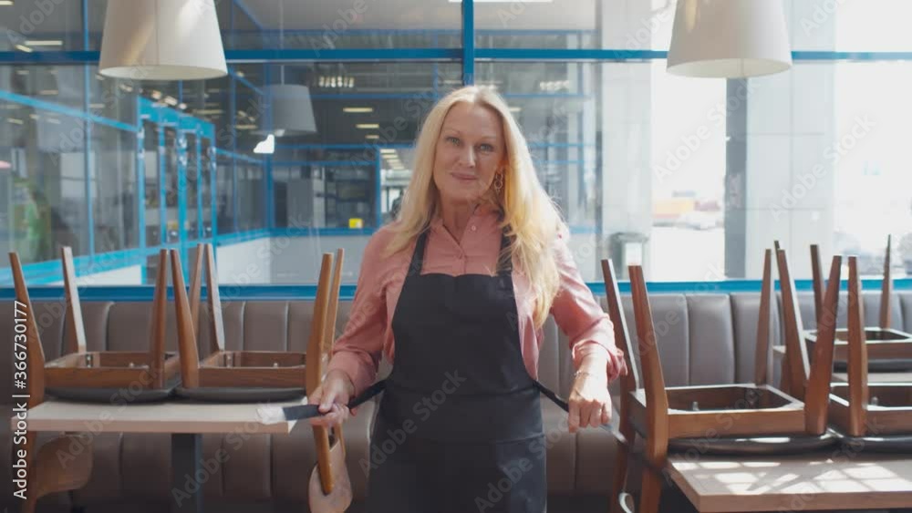 Senior happy cafe owner woman tie apron preparing to welcome guests in new cafe Senior happy cafe owner woman tie apron preparing to welcome guests in new cafe