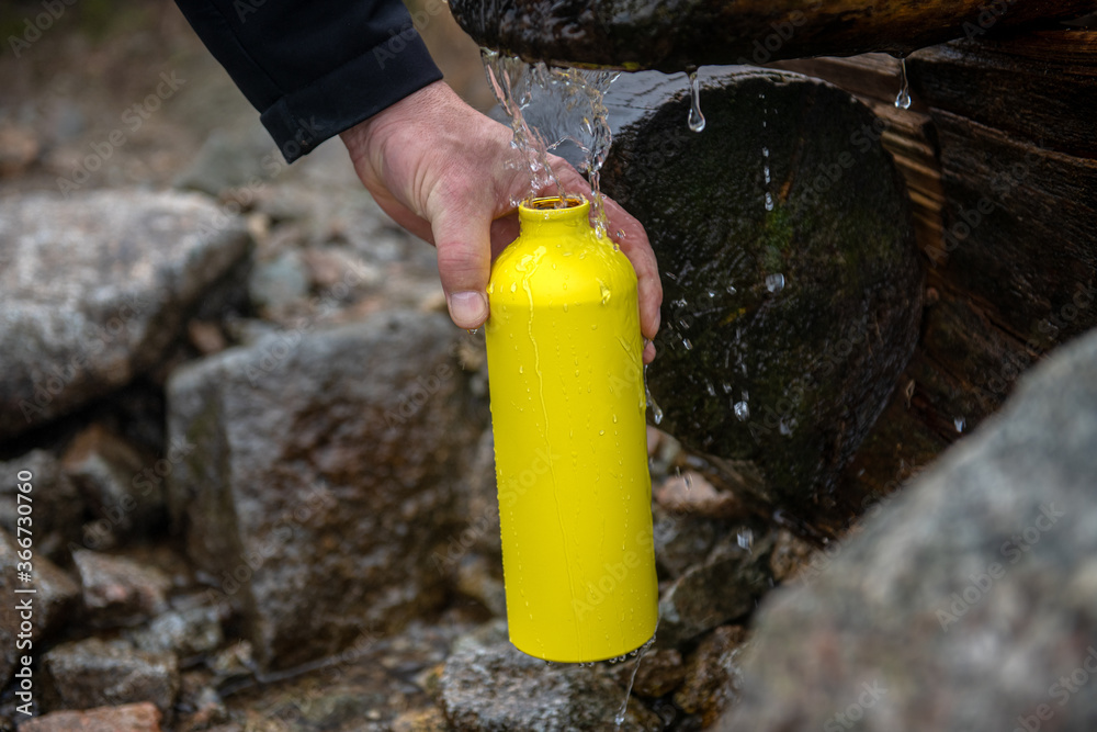 turysta napełniający żółtą metalowa butelkę wodą - obrazy, fototapety, plakaty 