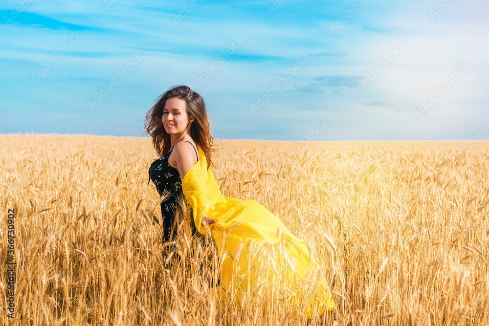 Naklejka premium A young girl with long hair and a yellow robe fluttering in the wind is dancing in a wheat field