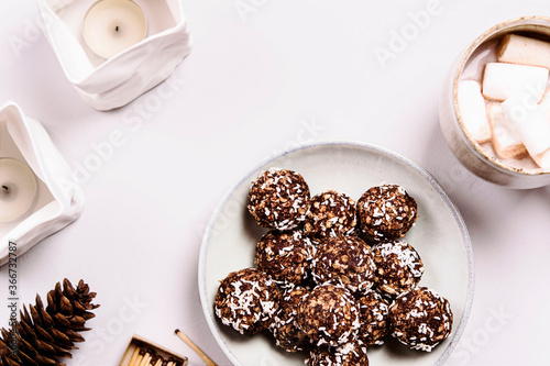 Swedish chocolate balls and cup of cocoa with marshmallow on grey concrete table. Cozy winter breakfast. Chokladbollar. Homemade healthy raw cocoa oatmeal balls sprinkled with coconut flakes photo