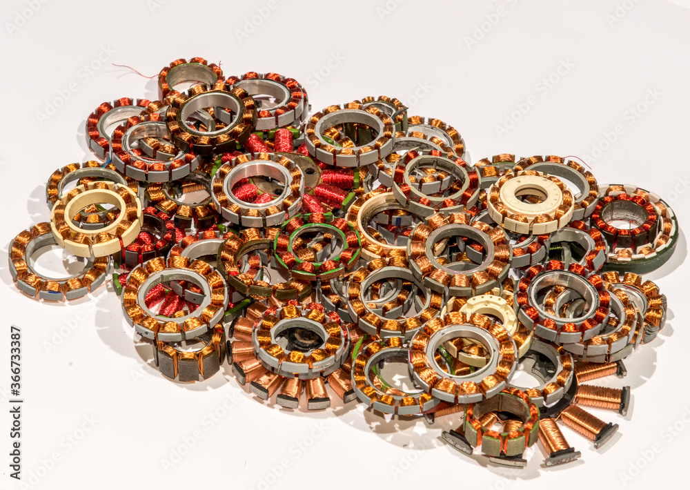 Coil assemblies from motors in hard drives and optical drives. The coils are in a pile to be recycled. They are wound with copper wire with red and clear enamel. View is from the top at an angle. Coil assemblies from motors in hard drives and optical drives. The coils are in a pile to be recycled. They are wound with copper wire with red and clear enamel. View is from the top at an angle.