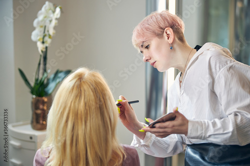 Attentive young woman doing makeup for her visitor