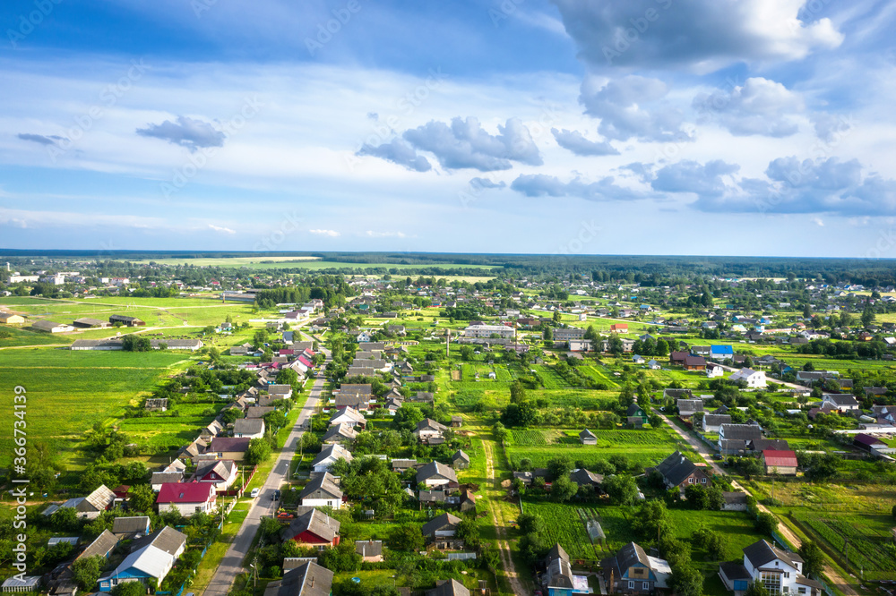 Fototapeta premium Aerial view village in summer sunny day. Picturesque view on fields, roofs of houses, forest, blue sky with clouds.