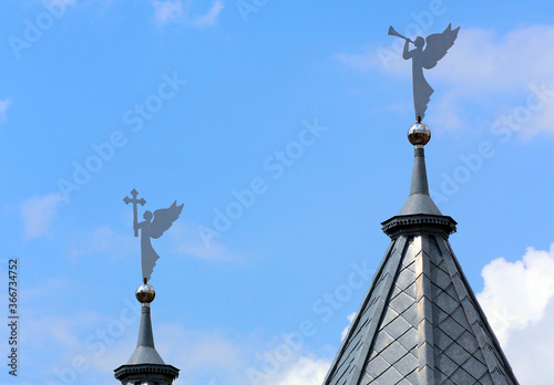 View of the roof of a Christian church with figurines of angels with wings holding a cross and a trumpet.