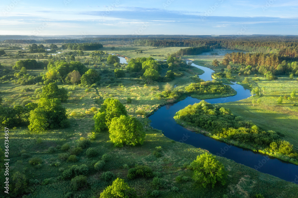 Aerial view of green meadow, river and forest. Summer sunrise. Sunrise over beautiful winding river.