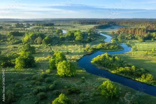 Aerial view of green meadow, river and forest. Summer sunrise. Sunrise over beautiful winding river.