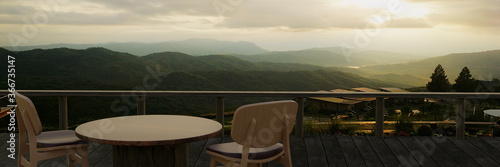 Wooden tables and chairs for relaxing on the balcony or terrace with wooden planks. The restaurant on the mountain has a hill and mist view in the morning sunlight. 3D Rendering