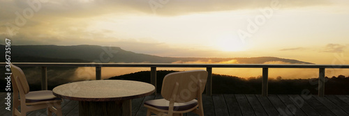 Wooden tables and chairs for relaxing on the balcony or terrace with wooden planks. The restaurant on the mountain has a hill and mist view in the morning sunlight. 3D Rendering © Superrider