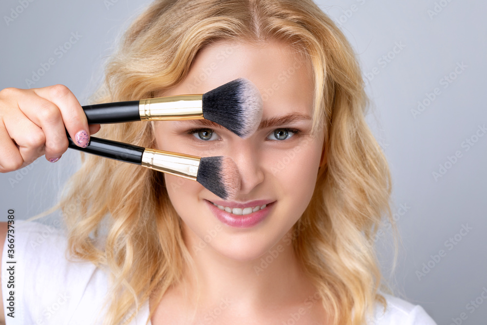 Portrait of a beautiful woman with curly blond hair, beautiful fresh makeup and healthy clean skin holding a powder brush in her hands. Professional makeup and skin care cosmetology. Portrait of a beautiful woman with curly blond hair, beautiful fresh makeup and healthy clean skin holding a powder brush in her hands. Professional makeup and skin care cosmetology.