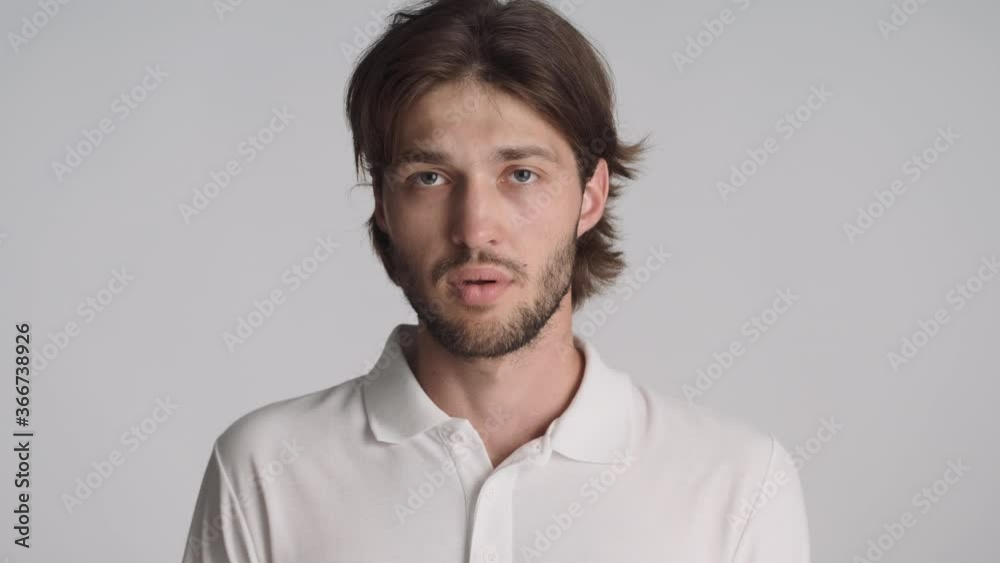 Portrait of young weary man doubtfully looking around posing on camera over gray background