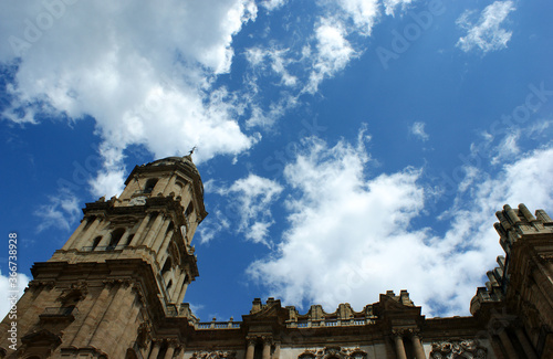 The beautiful cathedral of the historic city of Malaga. Angular view of the bell tower with ornate, decorative carvings.  Blue sky and clouds - copy space.