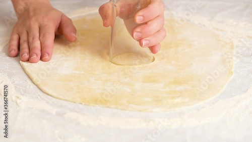 women's hands roll out the dough into dumplings, cuts out round pieces of dough with a glass.