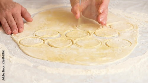 women's hands roll out the dough into dumplings, cuts out round pieces of dough with a glass.