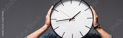 Panoramic crop of man holding clock near face isolated on grey, concept of time management