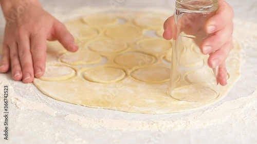 women's hands roll out the dough into dumplings, cuts out round pieces of dough with a glass.