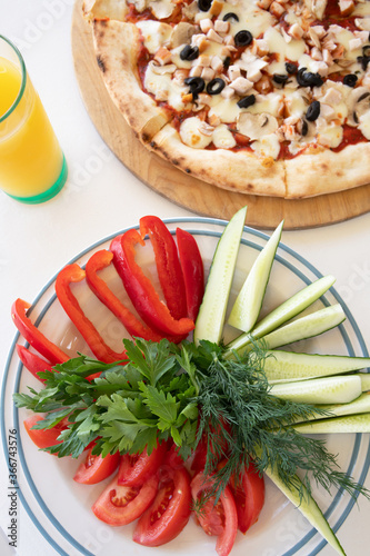 Pizza with olives and mushrooms and a plate of fresh vegetables