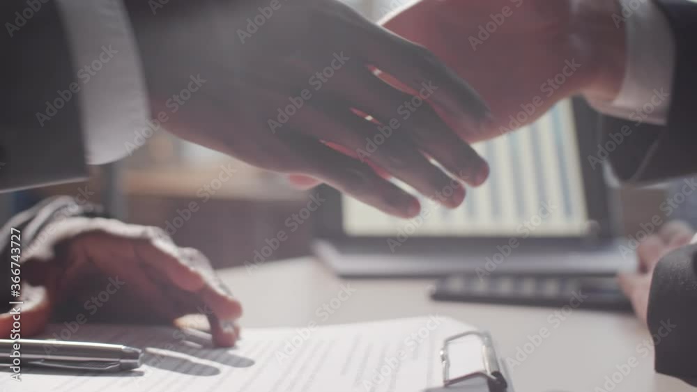 Close up view of hands of black entrepreneur in formalwear signing agreement and then giving handshake to male business partner
