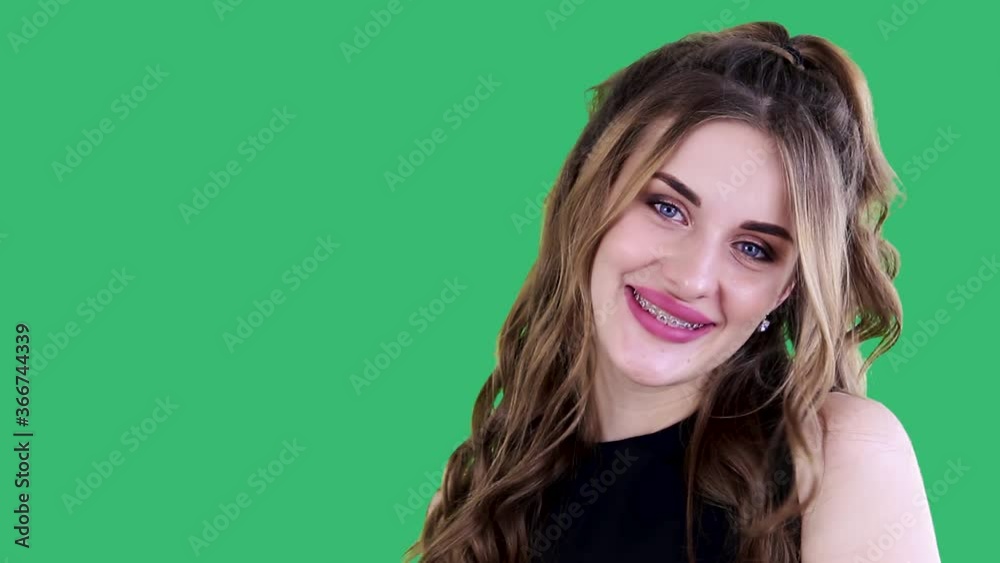 Charming,joyful young brunette smiling broadly,demonstrating her braces,dreaming about pleasant moments,looking at camera. Studio shot on green background. Health,beauty, dreaming,thought concept. Charming,joyful young brunette smiling broadly,demonstrating her braces,dreaming about pleasant moments,looking at camera. Studio shot on green background. Health,beauty, dreaming,thought concept.