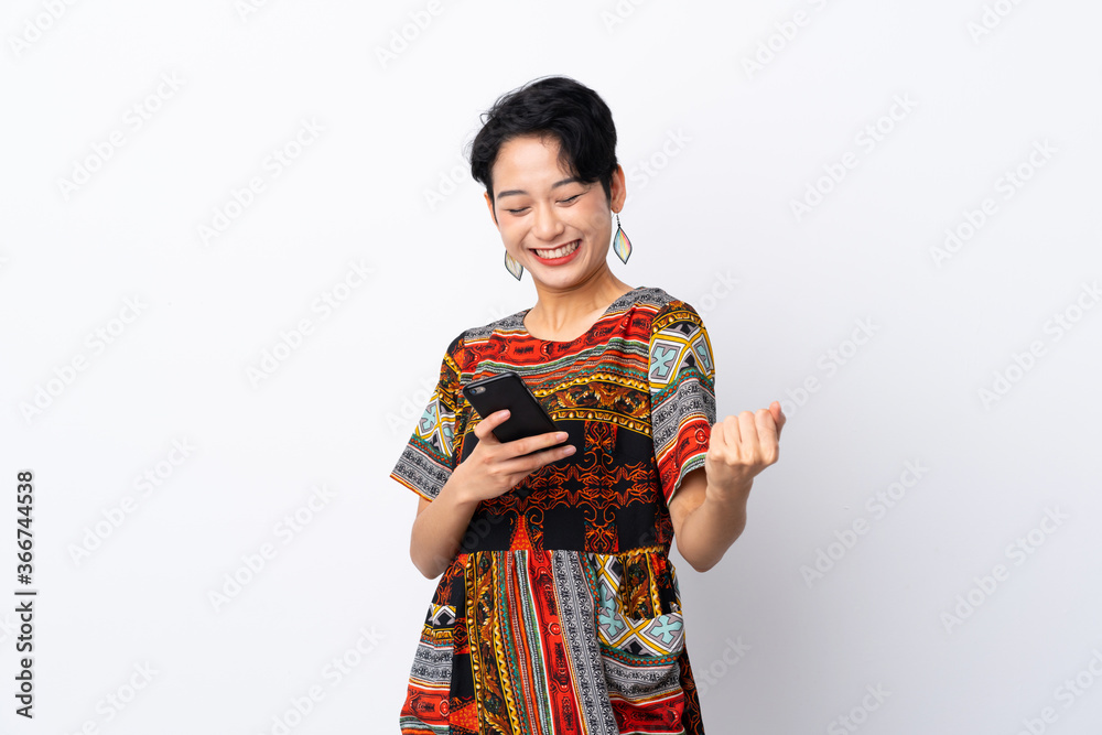 Young Asian girl with a colorful dress over isolated white background with phone in victory position Young Asian girl with a colorful dress over isolated white background with phone in victory position