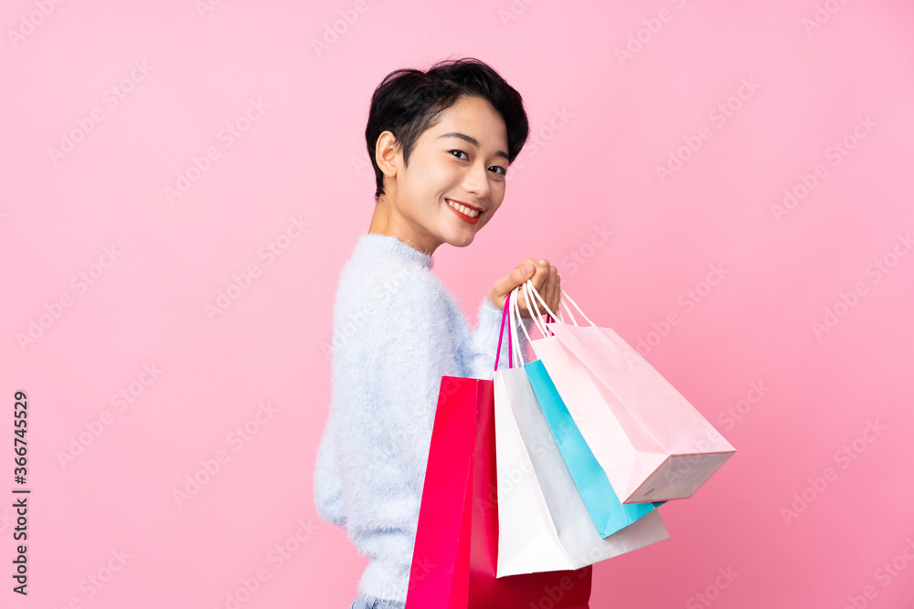 Young Asian girl over isolated pink background holding shopping bags and smiling Young Asian girl over isolated pink background holding shopping bags and smiling
