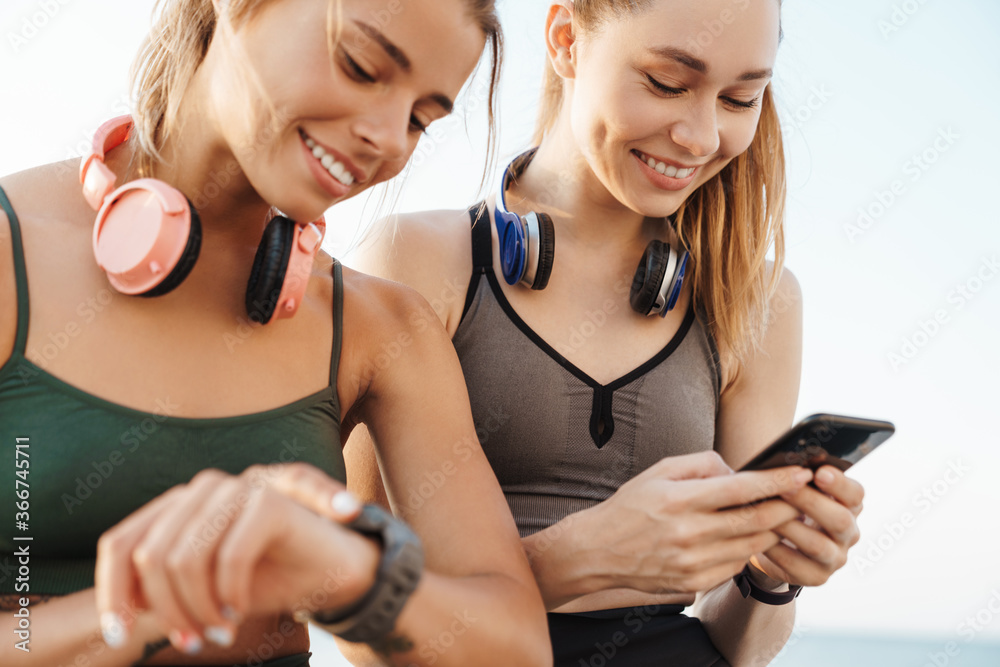 Sports women friends sitting outdoors using mobile phone Sports women friends sitting outdoors using mobile phone