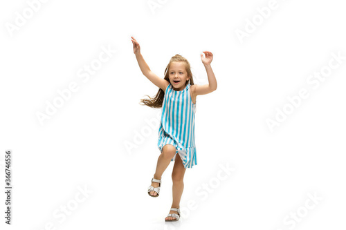 Happy child, little and emotional caucasian girl jumping and running isolated on white background. Looks happy, cheerful, sincere. Copyspace for ad. Childhood, education, happiness concept.