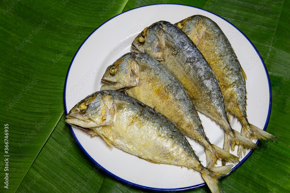 Fried steamed mackerel ripe, in white dish on green banana leaf Fried steamed mackerel ripe, in white dish on green banana leaf