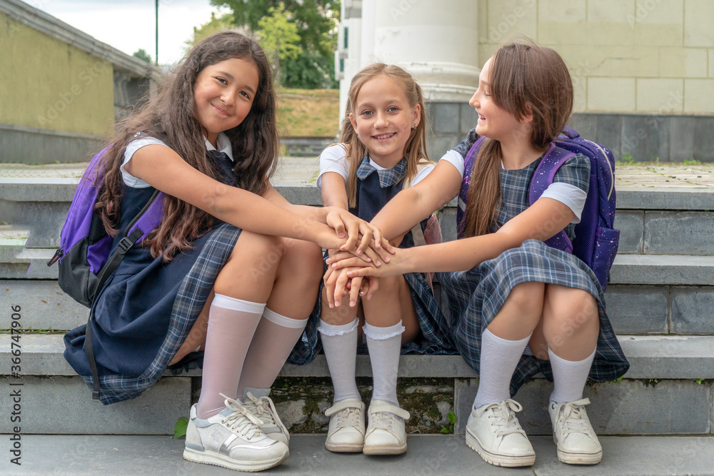 schoolkids school uniform are sitting on the stairs and holding hands. The concept of school friendship and happy children. foto de Stock Adobe