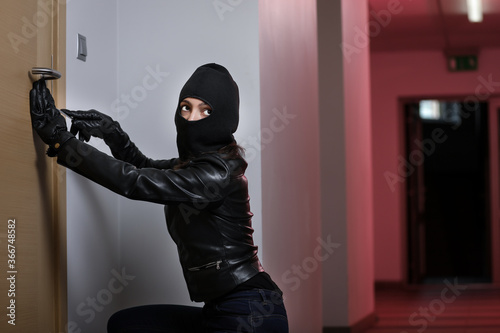 House robbery by woman in a black jacket and black mask. Burglar in a mask. Thief in a mask trying to break into other people's apartments © VItaliy