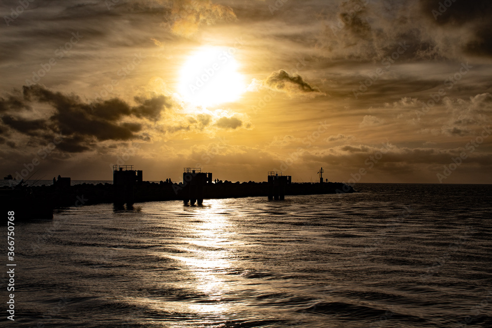 exciting backlight on the sea at the port of fiumicino; bright solar disc in a marine landscape with a yellow sky, shining sun on a swelling sea with silhouettes on the horizon; evening clouds 