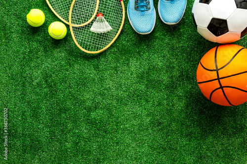 Sport games equipment - balls, sneakers, rockets - on grass top view copy space