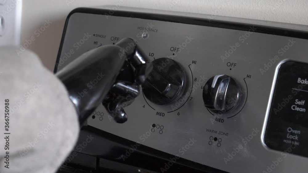 Young man with an artificial hand turning the knob of a stove oven to cook some food. Handicap person working with a fake limb. Closeup shot. Young man with an artificial hand turning the knob of a stove oven to cook some food. Handicap person working with a fake limb. Closeup shot.