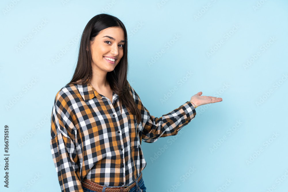 Young caucasian woman isolated on blue background extending hands to the side for inviting to come Young caucasian woman isolated on blue background extending hands to the side for inviting to come