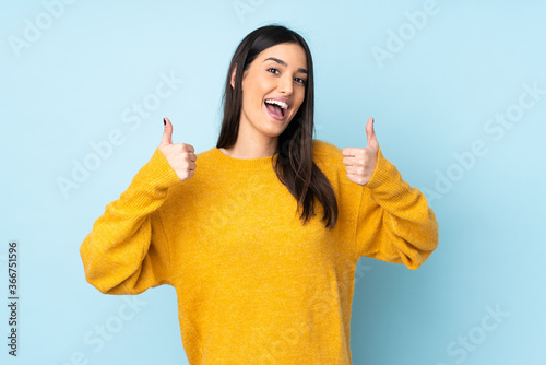 Foto Young caucasian woman isolated on blue background giving a thumbs up gesture