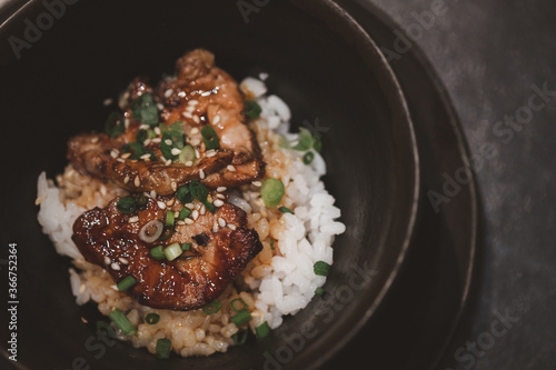 Grilled foie gras on top rice in black bowl.