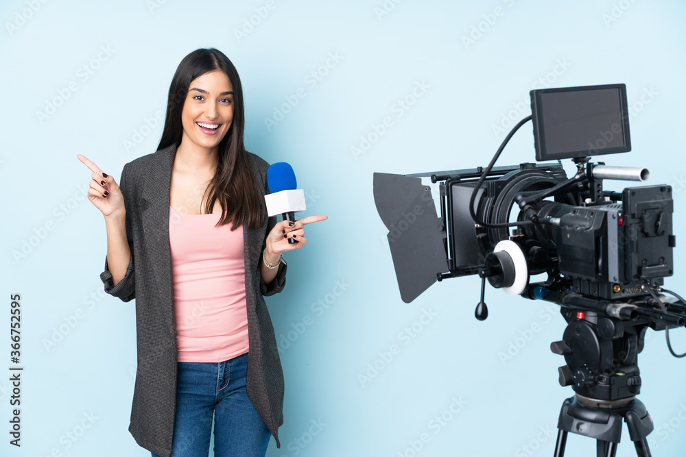 Reporter woman holding a microphone and reporting news isolated on blue background pointing finger to the laterals and happy Reporter woman holding a microphone and reporting news isolated on blue background pointing finger to the laterals and happy