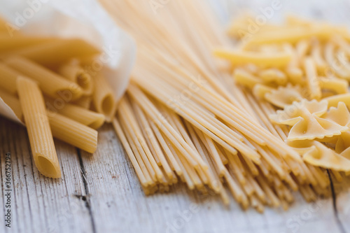 a lot of different kinds of egg noodles and yellow pasta on wooden background
