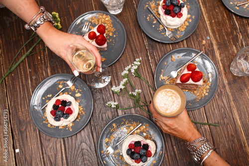 Bachelorette party, girls hands with drinks and sweet cakes with summer berries on a wooden table. Party, sweet table. Summer offer desserts in the restaurant.