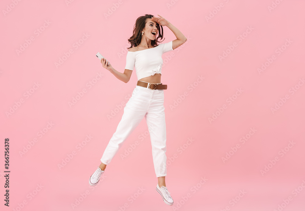 Image of cheerful brunette woman using cellphone while jumping