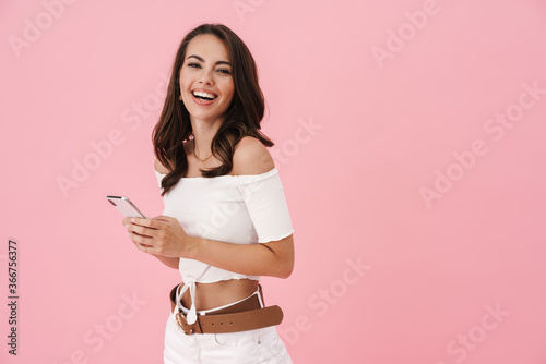Image of joyful brunette woman using cellphone and laughing