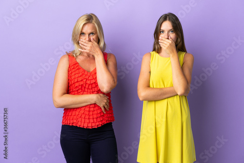 Mom and daughter isolated on purple background covering mouth with hands for saying something inappropriate