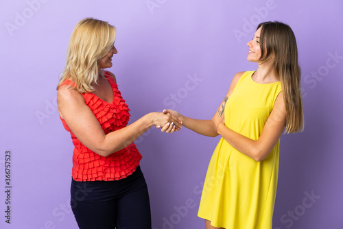 Mom and daughter isolated on purple background handshaking after good deal