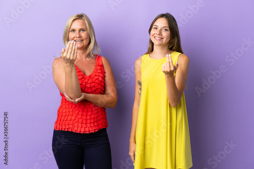 Mom and daughter isolated on purple background inviting to come with hand. Happy that you came
